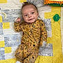 baby, infant, smile, onesie, leaf_pattern, quilt, blanket, plush_toy, pacifier, indoor, cute, child, sleepwear, happy, lying_down, cozy, soft_toy, patterned_clothing, toddler, face