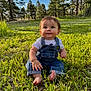 baby, barefoot, casual_clothing, child, curious, cute, daylight, denim_overalls, forest, grass, greenery, nature, outdoor, portrait, sitting, smile, summer, sunlight, trees, young_child