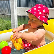 Axel is registered to the contest to win money with this photo: baby, ball, child, green_grass, inflatable, metal_wall, outdoor, playing, pool, red_hat, red_shorts, skin, summer, sunlight, sunny, toddler, toy, vacation, water, yellow_pool