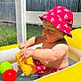 child, toddler, pool, inflatable, toy, red_hat, red_shorts, yellow_pool, water, ball, outdoor, summer, sunlight, playing, baby, skin, green_grass, metal_wall, sunny, vacation