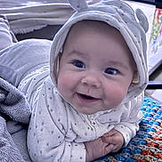 Lilas participe au concours pour gagner de l'argent avec cette photo : baby, blanket, blanket_texture, blue_eyes, cheeks, close_up, cozy, crochet_blanket, cute, fabric, hand, happy, home_interior, hood, hooded_onesie, infant, lying_down, plush_blanket, portrait, smiling