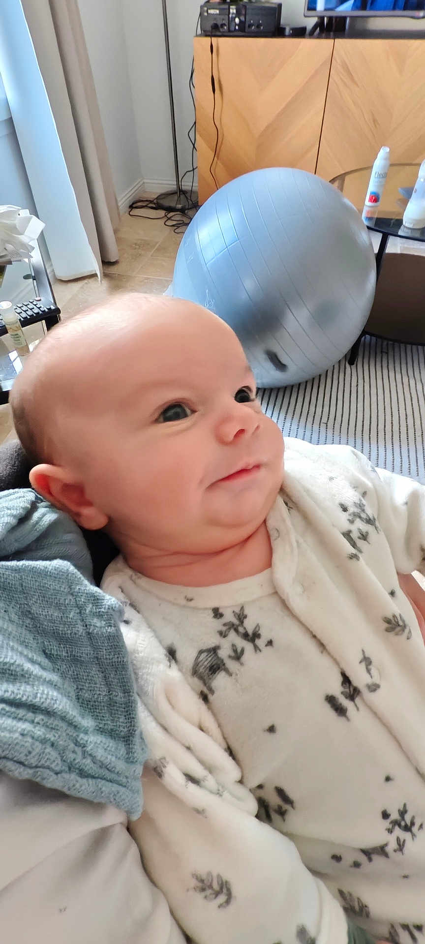 Elio participe au concours pour gagner de l'argent avec cette photo : baby, blanket, cabinet, carpet, child, clothing, curtains, exercise_ball, eyes, face, floor, furniture, head, home, indoor, infant, living_room, onesie, person, smile