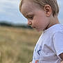 child, toddler, boy, side_profile, white_tshirt, bird_print, outdoor, field, grass, nature, sky, cloudy, portrait, casual_clothing, young_child, curly_hair, daytime, innocence, peaceful, candid