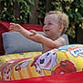 Noé participe au concours pour gagner de l'argent avec cette photo : toddler, child, inflatable_pool, pool_ring, cartoon_characters, outdoor, garden, greenery, cushions, red, yellow, blue, smiling, happy, water_drops, summer, playful, cute, baby, fun