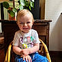 Noé participe au concours pour gagner de l'argent avec cette photo : toddler, child, smile, sitting, wicker_chair, indoor, plant, green_leaves, wooden_furniture, casual_clothing, blue_pants, white_tshirt, portrait, happy, cute, home_interior, natural_light, hands, face, young_child