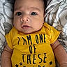 baby, infant, yellow_onesie, clothing, face, eyes, arms, blanket, pattern, cute, child, newborn, portrait, lying_down, soft_texture, skin, expression, indoor, person, small_hands