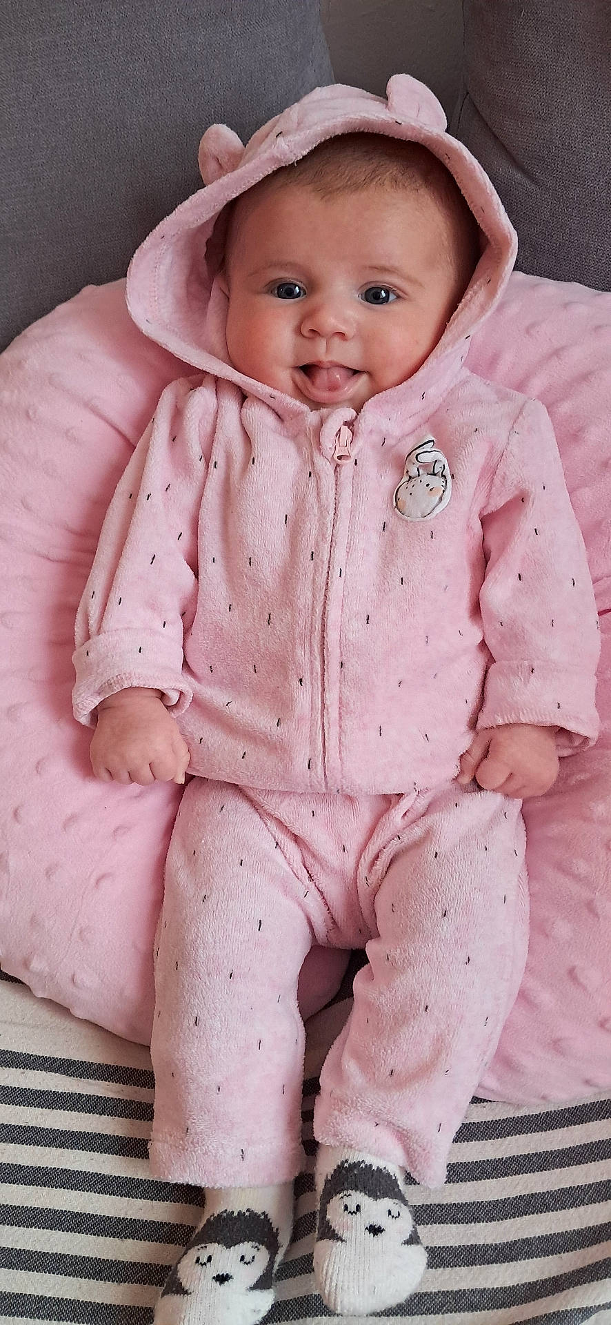 Camille a rejoint le concours — aidez-le/la à gagner de superbes lots ! baby, child, couch, cozy, cute, ears, happy, hood, indoor, infant, penguin_socks, pillow, pink_clothing, portrait, seated, smiling, socks, soft_fabric, tongue_out, young_child