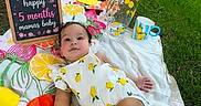 Khalessi is registered to the contest to win money with this photo: baby, blanket, chalkboard, child, clothing, cute, footwear, grass, infant, lemons, nature, outdoor, park, picnic, relaxing, sign, summer, sunlight, tree, willow_tree