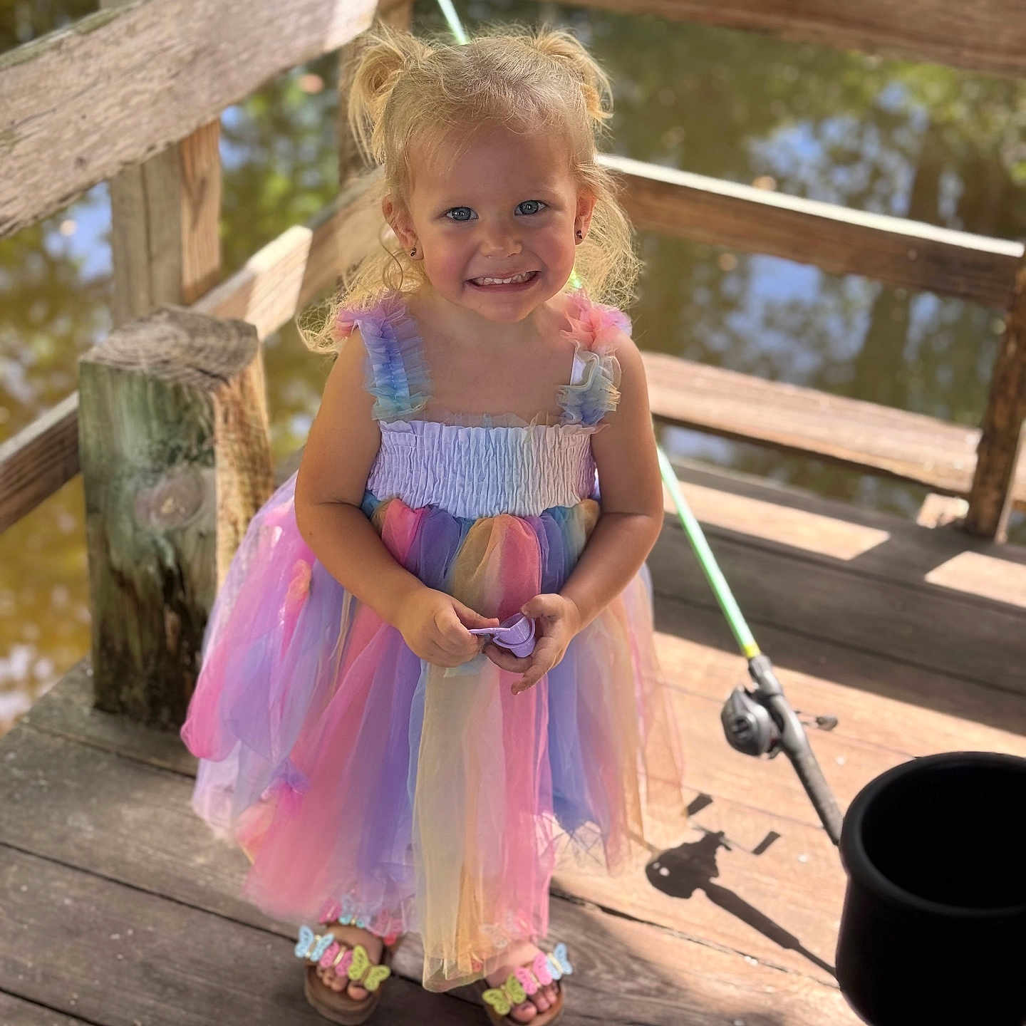 Paige is registered to the contest to win money with this photo: bucket, child, colorful, cute, dock, dress, fishing_rod, footwear, girl, happy, nature, outdoor, pigtails, playful, portrait, smiling, summer, sunlight, water, wooden