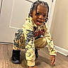 Kaison joined the competition — help win amazing prizes! child, indoor, crouching, tongue_out, braided_hair, hoodie, pants, black_sneakers, wooden_floor, door, wall, playful, smiling, person, young_child, cartoon_clothing, casual_wear, happy, cute, home