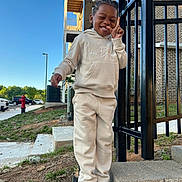 Kaison joined the competition — help win amazing prizes! child, smiling, casual_clothing, hoodie, sweatpants, sneakers, outdoor, daylight, blue_sky, brick_building, metal_fence, steps, grass, sidewalk, urban, playful, gesture, happy, person, parked_cars