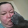 affectionate, cat, cheek, close_up, cuddle, face, fur, gray_cat, home, human_face, indoor, kiss, nasal_cannula, oxygen_tube, person, pet, portrait, selfie, wall, whiskers