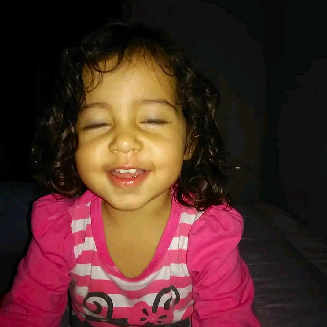 Kalytha is registered to the contest to win money with this photo: baby, casual_clothing, child, closed_eyes, curly_hair, cute, face, fun, happy, indoor, kid, long_sleeves, person, pink_shirt, portrait, sitting, smile, striped_clothing, toddler, young_child