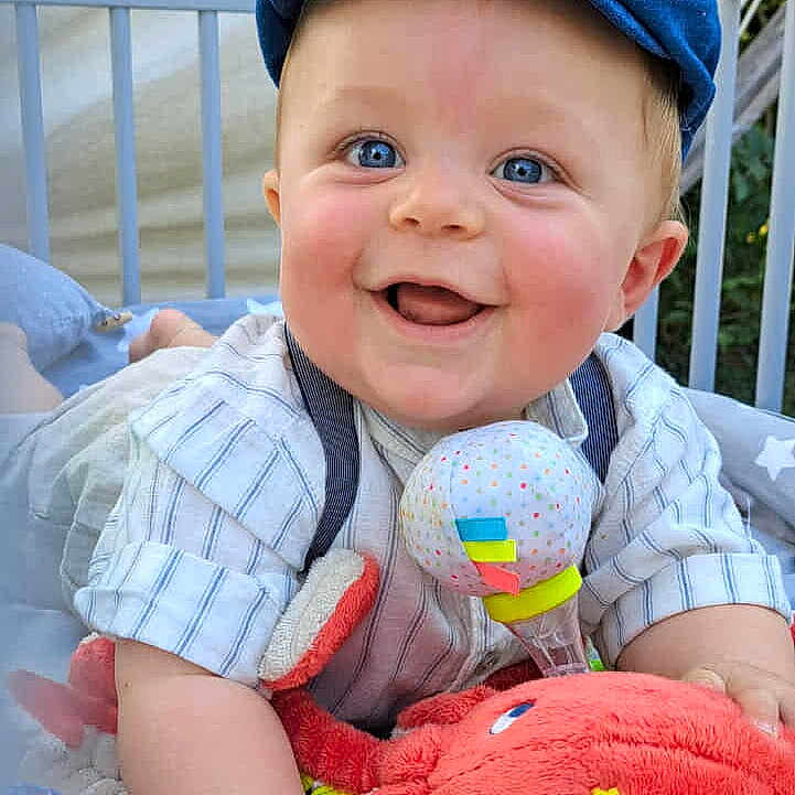 Tennessy a rejoint le concours — aidez-le/la à gagner de superbes lots ! baby, blue_eyes, cap, cheeky_grin, clothing, colorful_toy, crib, cute, expression, face, happy, indoors, infant, looking_at_camera, plush_toy, sitting, smile, soft_toys, toy, young_child