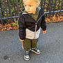 toddler, child, outdoor, pavement, jacket, hoodie, sneakers, stick, fence, grass, leaves, sidewalk, fall, casual_clothing, young_child, curious, standing, daylight, nature, portrait