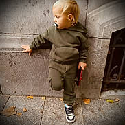 Leo a rejoint le concours — aidez-le/la à gagner de superbes lots ! toddler, child, pacifier, hoodie, cargo_pants, sneakers, side_view, wall, stone_pavement, fallen_leaves, urban, outdoor, holding_object, casual_pose, blond_hair, young_child, street, footwear, curious, daylight