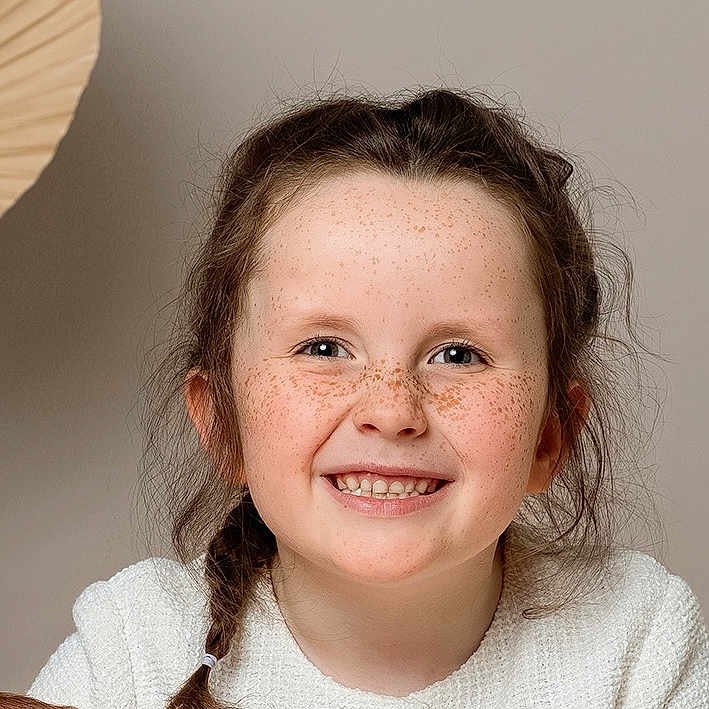 Elodie is registered to the contest to win money with this photo: braid, child, childhood, closeup, cute, expression, face, freckles, girl, hair, happy, indoor, joyful, natural_light, person, portrait, skin, smile, white_sweater, young