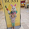 child, girl, bunny, costume, sign, mall, floor, tile, playful, hands, pose, spring, carrot, advertisement, jacket, boots, bow, cute, indoor, background