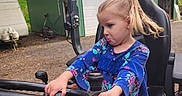 Lillian joined the competition — help win amazing prizes! blue_shirt, casual_clothing, child, flag, fun, girl, gravel, green_barn, nature, outdoor, play, pony_tail, propane_tanks, seat, serious_expression, steering_wheel, tractor, trees, vehicle, young