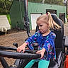 Lillian joined the competition — help win amazing prizes! child, girl, tractor, steering_wheel, blue_shirt, pony_tail, green_barn, outdoor, gravel, serious_expression, play, seat, vehicle, nature, trees, flag, propane_tanks, casual_clothing, young, fun