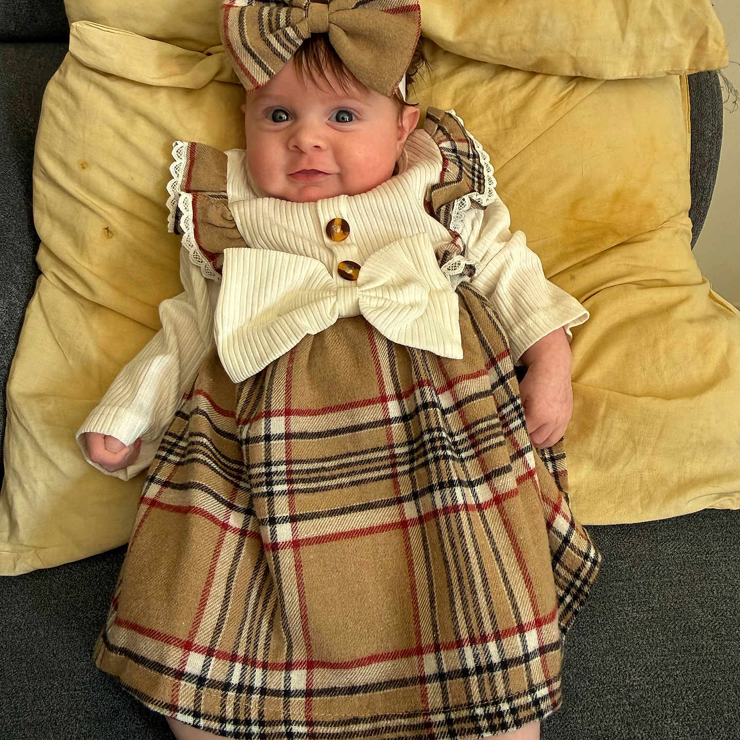 Noémie a rejoint le concours — aidez-le/la à gagner de superbes lots ! baby, child, infant, plaid_dress, bow_headband, yellow_cushion, smile, happy, cute, lying_down, indoor, soft_texture, portrait, small_hands, small_feet, clothing, headwear, cozy, adorable, person