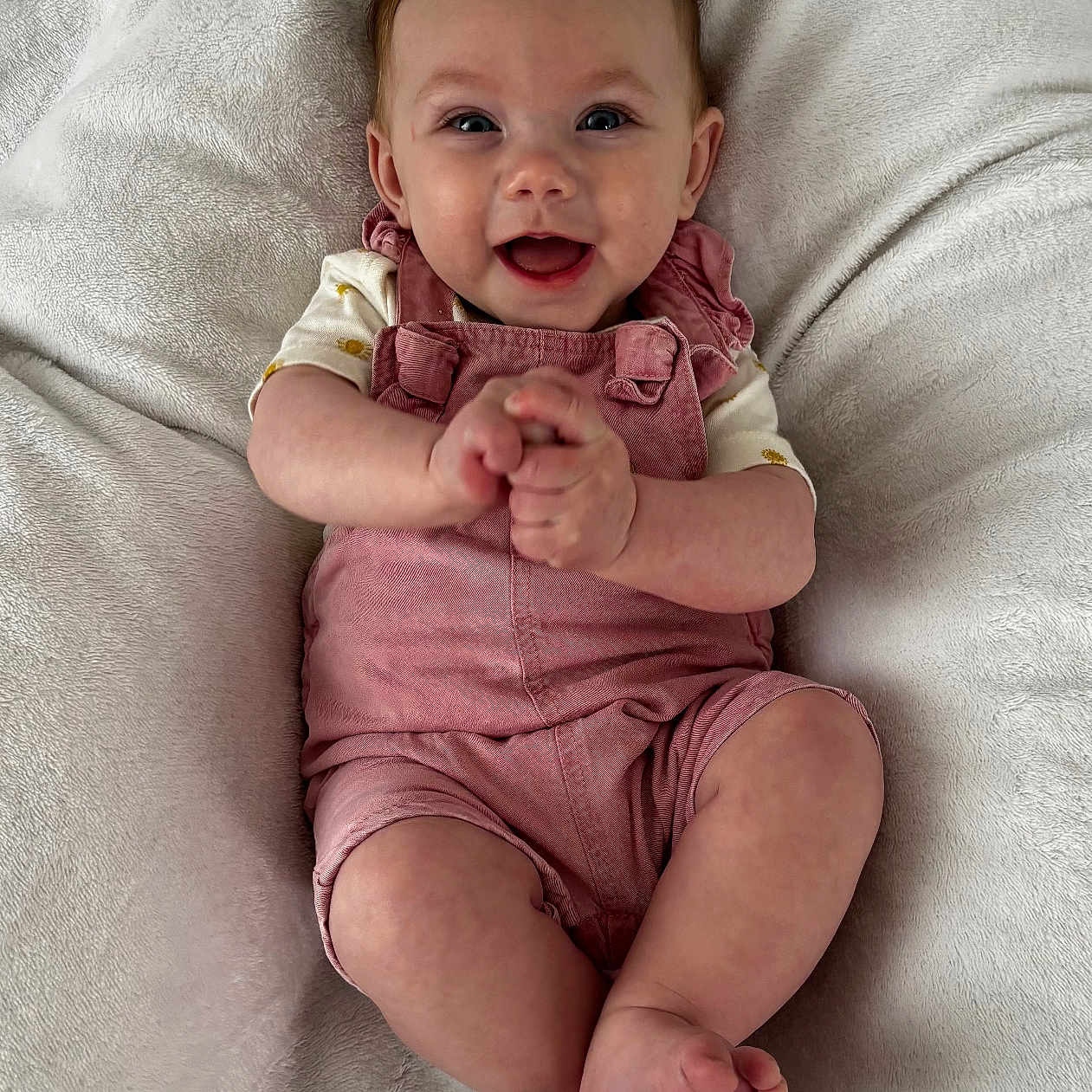 Lou participe au concours pour gagner de l'argent avec cette photo : baby, blanket, child, clapping, cozy, cute, expressive_face, feet, hands, happy, head, indoors, infant, laying_down, pink_overalls, portrait, skin, smiling, soft_texture, young_child