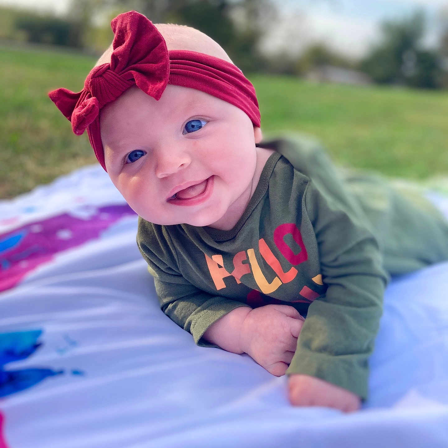 Brynlee is registered to the contest to win money with this photo: accessories, baby, blanket, bonnet, cap, clothing, face, grass, happy, hat, head, headband, hood, person, photography, plant, portrait, purple, quilt, smile
