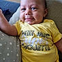 baby, child, smiling, yellow_shirt, text_on_clothing, pillow, star_pattern, cushion, indoor, portrait, person, infant, cute, relaxed, casual_clothing, human, young_child, comfortable, happy, closeup