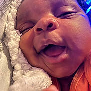 Alana joined the competition — help win amazing prizes! baby, close_up, face, smiling, sleeping, blanket, soft_texture, infant, joyful, mouth_open, cheeks, clothing, orange_shirt, resting, cozy, indoor, skin, head, cute, newborn