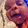 baby, close_up, face, smiling, sleeping, blanket, soft_texture, infant, joyful, mouth_open, cheeks, clothing, orange_shirt, resting, cozy, indoor, skin, head, cute, newborn