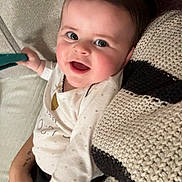 Talya participe au concours pour gagner de l'argent avec cette photo : baby, smiling, face, hand, knitted_blanket, cozy, indoor, person, child, happy, holding, textile, white_clothing, black_pants, couch, closeup, portrait, skin, infant, cute