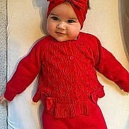 Aela joined the competition — help win amazing prizes! baby, child, red_clothing, headband, bow, knitwear, smile, portrait, indoors, cute, infant, face, person, lying_down, warm_clothing, young_child, adorable, soft_surface, baby_girl, fashion