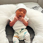 Jakor joined the competition — help win amazing prizes! newborn, baby, infant, hat, white_clothing, dinosaur_print, cushion, pillow, sleepy, yawning, cozy, indoors, wooden_background, cute, small_hands, white_socks, lying_down, resting, soft_texture, child