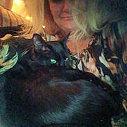 Bynxzie is registered to the contest to win money with this photo: person, cat, black_cat, indoor, low_light, couch, blonde_hair, animal, pet, face, relaxing, close_up, furniture, home, portrait, cozy, companion, casual, resting, warm_lighting