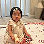 baby, child, girl, plush_toy, duck, dress, hair_clip, flower_pattern, blanket, carpet, indoor, sitting, cute, infant, soft_toy, foot, face, person, decor, cozy