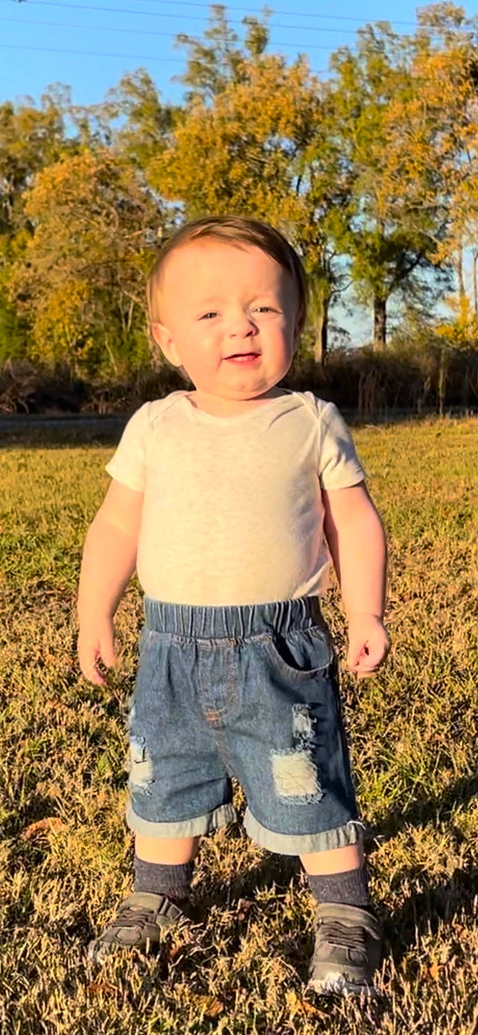 Jonathan is registered to the contest to win money with this photo: baby_toddler_clothing, blond, child, cool, face, fun, gesture, grass, happy, head, people_in_nature, person, plant, shorts, sleeve, smile, sunlight, t_shirt, toddler, tree