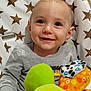 baby, child, smiling, face, plush_toy, high_chair, star_pattern, clothing, gray_shirt, indoor, happy, cute, young_child, person, portrait, seat, toy, colorful, infant, expression