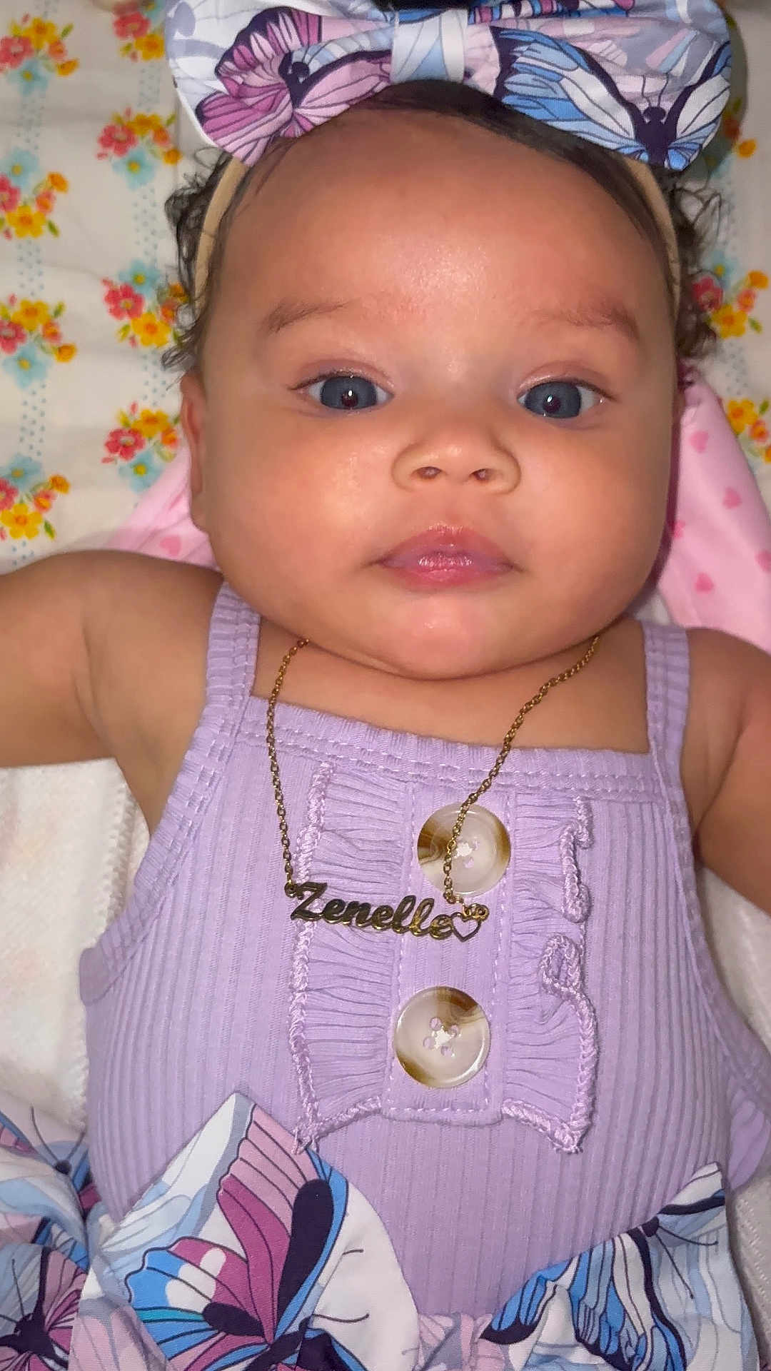 Zenelle is registered to the contest to win money with this photo: baby, child, face, portrait, blue_eyes, headband, bow, necklace, jewelry, purple_outfit, buttons, butterfly_pattern, clothing, infant, cute, closeup, skin, person, laying_down, adorable