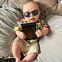 baby, sunglasses, passport, floral_shirt, shorts, bed, pillow, plush_headboard, infant, person, cute, relaxing, indoors, child, hand, foot, casual_clothing, portrait, travel, accessory
