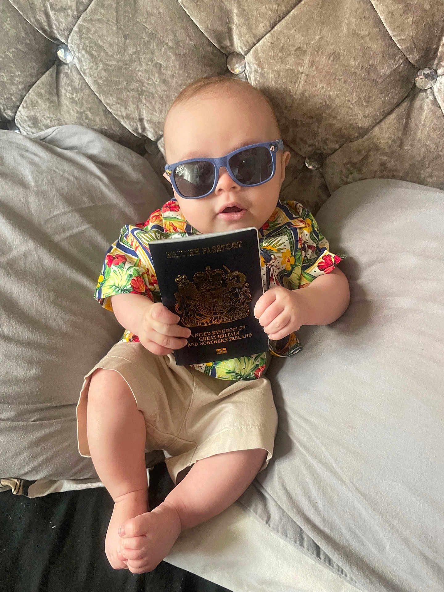 Harley joined the competition — help win amazing prizes! baby, sunglasses, passport, floral_shirt, shorts, bed, pillow, plush_headboard, infant, person, cute, relaxing, indoors, child, hand, foot, casual_clothing, portrait, travel, accessory
