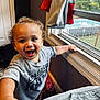 toddler, child, smiling, curly_hair, indoor, window, shirt, reaching_hand, happy, daylight, jacket, bedroom, carpet, home, person, furniture, playful, young_child, expression, casual_clothing