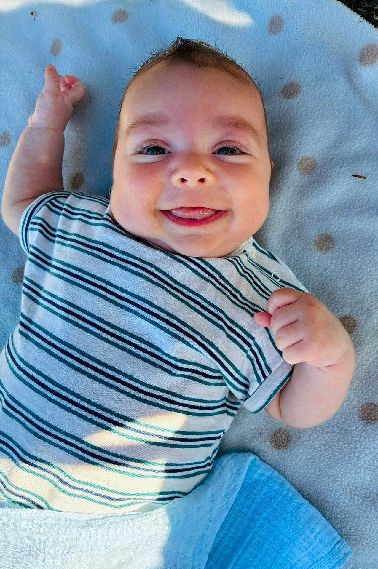 Dilan is registered to the contest to win money with this photo: baby, smiling, striped_shirt, blanket, polka_dots, face, infant, happy, tongue_out, lying_down, cute, child, skin, hand, outdoor, daylight, head, eyes, clothing, soft