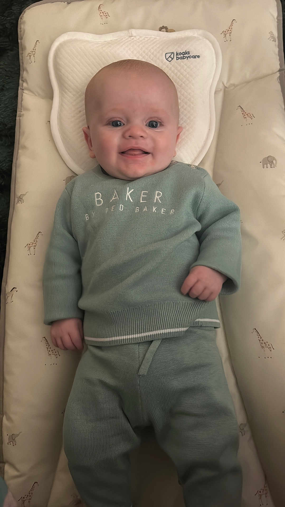 Oliver is registered to the contest to win money with this photo: baby, infant, smiling, lying_down, baby_mat, giraffe_pattern, elephant_pattern, green_clothing, sweater, pants, face, head, hands, cozy, indoor, cute, child, person, happy, soft
