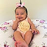 baby, infant, pink_bow, smiling, cute, floral_pillow, wooden_sign, three_months, child, portrait, indoors, happy, sitting, feet, hand, clothing, person, head, skin, young
