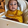 Adelina joined the competition — help win amazing prizes! baby, child, high_chair, yellow_bib, food, messy, surprised, hair_tie, pony_tail, indoor, kitchen, face, expression, cute, infant, person, feeding, table, seat, cloth