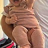 baby, child, smiling, happy, knitted_clothing, pink, person, indoor, adult_hand, waving, cute, infant, portrait, sleeveless, pants, barefoot, holding, fabric, face, young