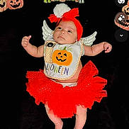 Amira joined the competition — help win amazing prizes! adorable, baby, bib, black_background, celebration, child, costume, cute, decorations, festive, halloween, headband, holiday, holiday_clothing, holiday_theme, infant, infant_clothing, lying_down, pumpkin, red_tutu