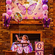 Miley is registered to the contest to win money with this photo: toddler, child, high_chair, balloon, birthday, party, decoration, purple, pink, butterfly, banner, unicorn, celebration, wooden, dress, festive, indoor, blocks, smiling, happy