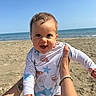 baby, child, beach, ocean, sea, water, sand, sunny, blue_sky, swimsuit, patterned_clothing, smiling, happy, person, holding, arm, summer, vacation, outdoor, portrait
