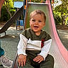toddler, child, smiling, slide, playground, outdoor, trees, sunlight, greenery, clothing, happy, person, park, footwear, hand, face, sitting, metal_slide, casual_wear, nature